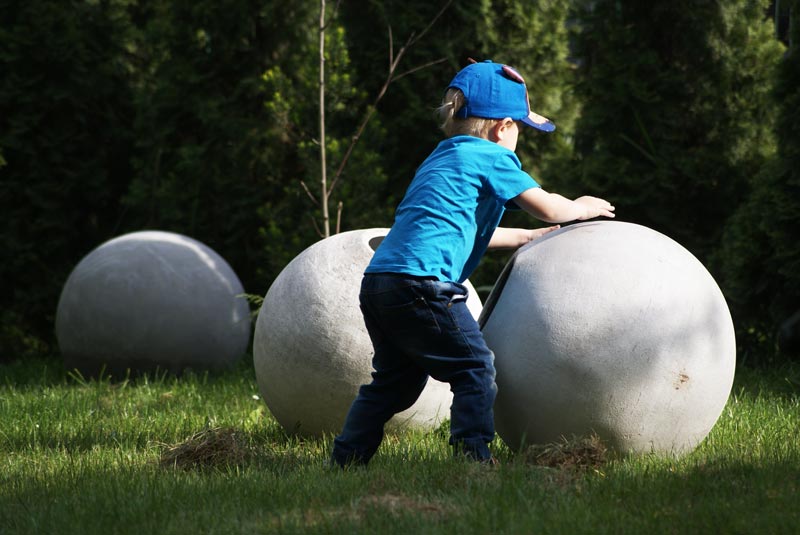 Chłopiec przetaczający lekkie kule betonowe ogrodowe